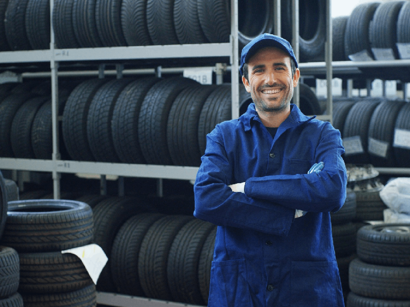 Mecánico sonriente con estanterías de neumáticos al fondo